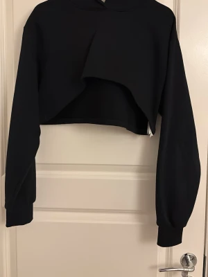 Svart cropped hoodie - Säljer en svart cropped hoodie. Hoodien har en klassisk huva och breda muddar vid ärmsluten. Perfekt för dig som gillar streetwear och vill ha en unik look. Materialet känns mjukt och stretchigt.
