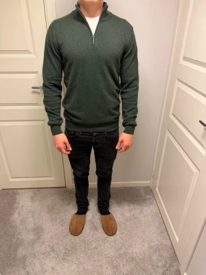 Mörkgrön half zip tröja  - Mörkgrön långärmad tröja med half zip och hög krage. Tröjan har ribbade muddar vid ärmslut och nederkant, vilket ger en snygg och bekväm passform. Perfekt för dig som gillar stilrena och enkla plagg. Ts Ai