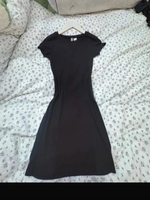 Svart kortklänning från H&M Divided - En svart, enkel och figurnära kortklänning från H&M Divided. Klänningen har rund halsringning och korta ärmar. Tillverkad i mjuk bomull som känns skön mot huden. Perfekt basplagg att styla på olika sätt.