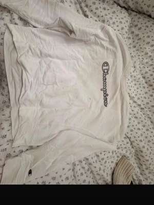 Vit sweatshirt från Champion - Säljer en vit sweatshirt från Champion med det klassiska Champion-loggan tryckt på bröstet i svart. Tröjan har rund halsringning och muddar vid ärmslut och nederkant. Perfekt för en avslappnad och sportig stil.