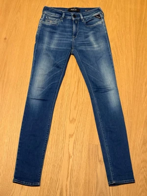 Blå Replay skinny jeans - Säljer ett par blå skinny jeans från Replay med klassisk femficksdesign och snygga slitningar framtill. Jeansen har normal midja och är tillverkade i stretchigt bomullsmaterial för skön passform. Perfekta till din vardagsstil!