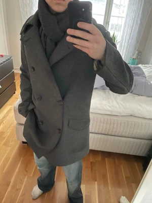 Mörkgrå skepparkavaj från Tommy Hilfiger  - Stilren mörkgrå skepparkavaj från Morris med dubbelknäppning och bred krage. Klassisk modell i ullblandning, perfekt för kyliga dagar. Två framfickor och en bröstficka ger en tidlös look. Passar till både jeans och mer dressade outfits.