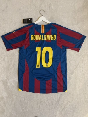 Ronaldinho matchtröja - Säljer en klassisk FC Barcelona matchtröja från Nike med Ronaldinho och nummer 10 på ryggen. Tröjan har blå och vinröda vertikala ränder, gula detaljer och klubbmärke på bröstet. 