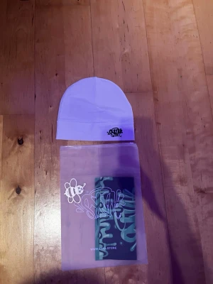 Vit mössa från Syna - Snygg vit mössa från Syna med minimalistisk design och svart logga broderad framtill. Tillverkad i mjukt och stretchigt material som sitter skönt på huvudet. Perfekt accessoar för att lyfta din streetwear-look.