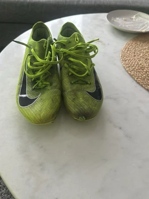 Nike gröna fotbollsskor med snörning - Snygga limegröna Nike fotbollsskor med svart swoosh på sidan och snörning. Skorna har en låg profil och är tillverkade i syntetmaterial för bästa känsla på planen. Perfekta för dig som vill sticka ut på fotbollsplanen.