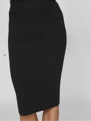 Svart ribbad stickad kjol - Snygg svart stickad kjol med ribbad struktur och kroppsnära passform. Kjolen är midilång och passar perfekt till både sneakers och boots. Enkel att styla med en oversized tröja eller en tight topp.