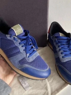 Blå Valentino Rockrunner sneakers - Snygga blå Valentino Rockrunner sneakers med ovandel i mesh och mocka, samt detaljer i skinn. Skorna har klassisk snörning och en beige sula som ger en sportig look. Perfekta för dig som vill ha stilrena och trendiga sneakers.