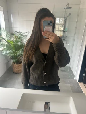 Mörkgrå kofta med blommiga knappar - Mysig mörkgrå kofta med v-ringning och tre dekorativa blommiga knappar framtill. Koftan har långa ärmar och bred ribbstickning vid ärmslut och nederkant. Stl M men passar lika bra som S. Hör av er vid frågor❤️