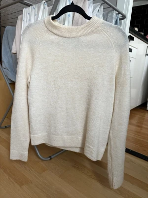 Krämvit stickad tröja Vero Moda - Mysig krämvit stickad tröja från Vero Moda med rund halsringning och ribbade muddar vid ärmslut och nederkant. Tröjan har en enkel och stilren design. Materialet är mjukt och behagligt.