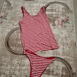 Rödvit randig bikini med linne - Säljer en bikini med rödvita ränder, består av ett linne med smala axelband och matchande bikinitrosa. Snygg och lekfull design som sticker ut på stranden. Materialet känns mjukt och stretchigt, perfekt för sommardagar vid vattnet.