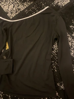 Svart topp med lång ärm - Svart topp med lång ärm och vit kant upptill. 