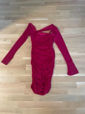 Röd omlottklänning med cut out - Trendig röd kortklänning med lång ärm och snygg cut out-detalj vid halsen. Klänningen har omlott-effekt och rynkade partier längs sidorna för en smickrande siluett. Perfekt för dig som vill sticka ut med en unik och modern look.