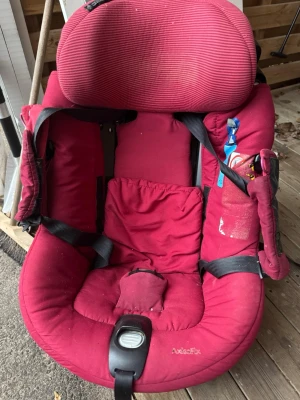 Röd bilbarnstol Axkid med ISOFIX - Säljer en röd bilbarnstol från Axkid med ISOFIX-fäste. Stolen har vadderad sits, justerbara säkerhetsbälten och tydliga instruktioner på sidan. Passar barn upp till 19 kg och har fickor för småsaker. Perfekt för säker bilfärd.