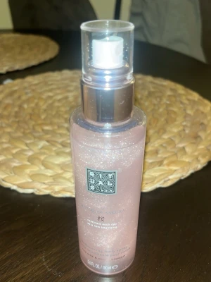 Rituals The Ritual of Sakura Body Spray - En lyxig body mist från Rituals, The Ritual of Sakura, i en rosa skimrande flaska med silvrig spraypump. Den glittrar på kroppen. Doften är inspirerad av japansk körsbärsblom och flaskan rymmer 150 ml. Perfekt för dig som vill ha en fräsch och blommig doft. Har endast testsprayat den så hela flaskan är i princip kvar.