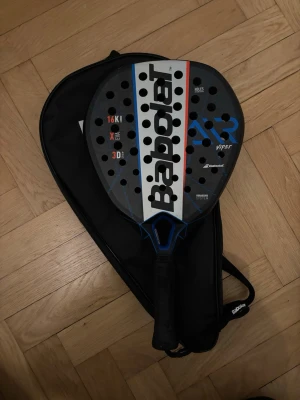 Babolat Viper padelracket med fodral - Säljer ett Babolat Viper padelracket i svart med blå och röda detaljer. Racket har hålmönster och tydlig logga på framsidan. Medföljer ett svart fodral med dragkedja och axelrem. Perfekt för dig som gillar padel.