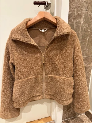 Brun teddyjacka från h&m - Mysig brun teddyjacka från h&m, använd runt 5 gånger men ser nästan helt ny ut. Jackan har en rak, något croppad passform och stängs med dragkedja framtill. Pris kan diskuteras!