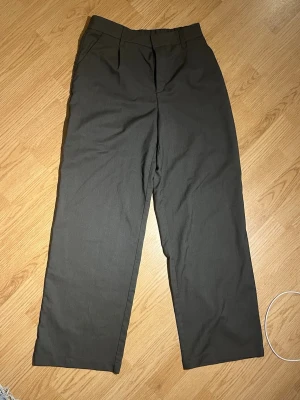 Mörkgrå kostymbyxor med raka ben - Stilrena mörkgrå kostymbyxor med klassisk passform och raka ben. Byxorna har hällor för bälte och diskreta sidfickor. Perfekta för en dressad look och enkla att matcha med skjorta eller t-shirt.