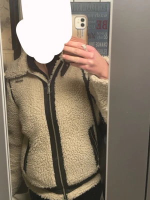 Beige teddyjacka med svarta detaljer - Säljer en beige teddyjacka med svarta detaljer och dragkedja framtill. Jackan har hög krage, markerade sömmar och fickor med svarta kanter🥰