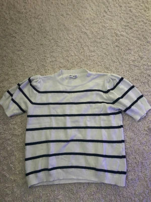 Vit och marinblå randig topp - Kortärmad topp från Meet me there i vit med marinblå horisontella ränder. Rund halsringning och mjukt stickat material som ger en avslappnad men ändå stilren look. Perfekt till jeans eller kjol för en fräsch outfit.