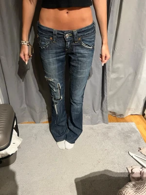 True religion jeans - Säljer ett par blå bootcut jeans med slitna detaljer och kontrastsömmar. Jeansen har låg midja och coola fickor bak med dekorativa sömmar. Perfekta för dig som gillar en avslappnad och trendig stil. Köpte dom här på Plick för länge sen för ca 1000 kr. Dom var hyffsat dyra eftersom true religion är ett dyrt märke. Säljer för att dom ej kommit till användning.