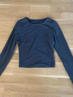 Grå långärmad topp - En enkel och stilren mörkblå långärmad topp med rund halsringning. Toppen har en croppad passform och är tillverkad i ett mjukt och stretchigt material som känns skönt mot huden. Perfekt att matcha med jeans eller kjol.