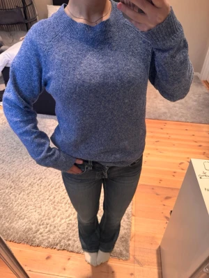 Blå stickad tröja i ullmix från Vero Moda  - Mysig blå stickad tröja med rund halsringning och långa ärmar. Tröjan har en melerad look och ribbstickade muddar vid ärmslut och nederkant. Perfekt för kalla dagar och enkel att matcha med jeans.