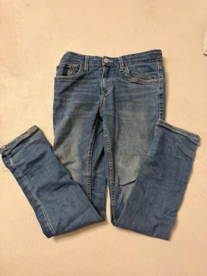 Levi's 512 blå jeans slim fit - Ett par klassiska blå Levi's 512 jeans med straight fit och femficksmodell. Jeansen har normal midja, ljus tvätt och är tillverkade i slitstark bomullsdenim. Perfekta för en avslappnad och tidlös look.