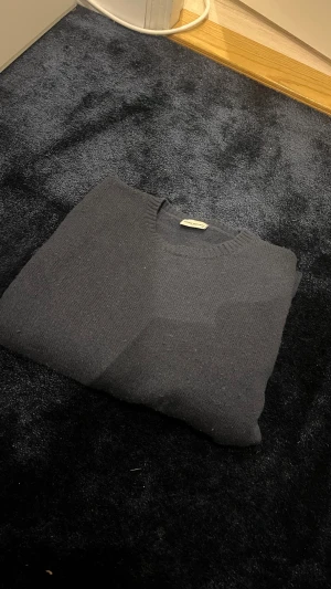 Svart stickad tröja John Henric - Klassisk svart stickad tröja från John Henric med rund halsringning och ribbstickade muddar. Perfekt för lager-på-lager och enkel att matcha med olika outfits. Tillverkad i mjukt material som känns skönt mot huden.