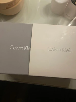 Calvin Klein halsband med cirkel & fyrkant - Snyggt halsband från Calvin Klein med en tunn silverfärgad kedja och två hängen: en rund ring i guldton och en fyrkant i silver. Stilren och modern design, perfekt för dig som gillar minimalistiska smycken. Levereras i originalask. I rostfritt stål.