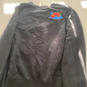 Svart tröja från Nike - En svart tröja från Nike med färgglatt tryck på ryggen som säger 'Have a Nike Day'. Tröjan har långa ärmar och en normal passform.