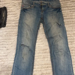 snygga lågmidjade jeans - lågmidjade jeans med hål och dem sitter i en rak modell så att dem går över skorna 