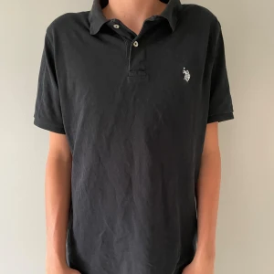 Svart pikétröja  - En fin US polo pike i toppskick, inga fläckar, hål eller andra defekter. Modellen på bilden är 185