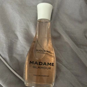 Madame Glamour Eau de Parfum - En elegant flaska med Madame Glamour Eau de Parfum från Suddenly Fragrances. Parfymen har en ljusrosa vätska och kommer i en genomskinlig glasflaska med en vit kork.