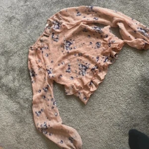 Blommig blus från Petites - En blommig blus från Petites i en ljusrosa färg med blå blommönster. Blusen har långa ärmar och volangdetaljer vid ärmslut och nederkant.