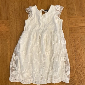 Vit klänning - Gullig vit klänning med vita blommor. Bild 1: framsidan  Bild 2: baksidan  Bild 3: motivet  Nästan aldrig använd, är från Kappahl i storlek 104