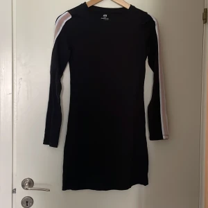 Svart klänning från H&M - En svart klänning från H&M Basic tillverkad av ekologisk bomull. Klänningen har långa ärmar med dekorativa ränder i silver, vit och rosa längs ärmarna.