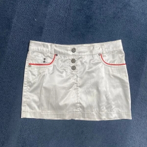 Mini skirt - Mini skirt i vitt blankt material med röda detaljer. Storlek 34, midjemått: ca 37 cm, stretchigt material☺️