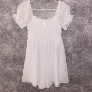 Klänning med insydda shorts - En vit och fin klänning med ”insydda” shorts och skönt, strechigt material som sitter åt rund midjan. Materialet på klänningen är tunnt och skönt. Den har en rosett där fram, den är helt oanvänd och därför inga slitningar👍