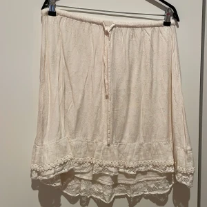 Knälång kjol med en liten spets nedtill från Creme - Romantisk kjol till knäna och skön resår i midjan med knyt, mycket fint skick och normal i storlek.