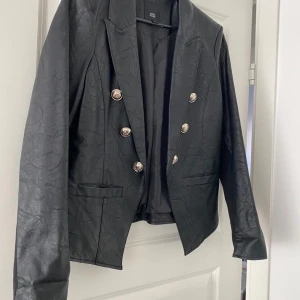 Svart läder jacka nyskick! - Snygg kaval/jacka från River island i storlek UK 12 (passar storlek M) i svart läder imitation med guldiga knappar. Väldigt lite använd. Fint skick.
