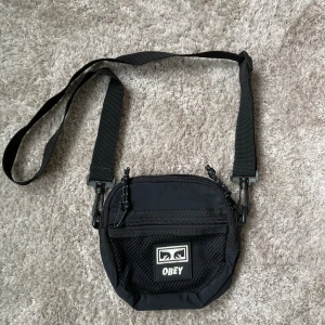 Axelväska obey - Svart axelväska från obey.