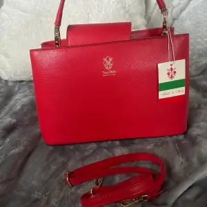 En fin röd väska i läder köpt i Italien oanvänd med band och prislapp, stor o rymlig med fack i!