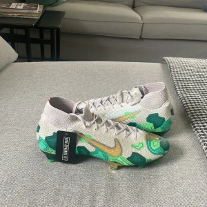 Nike Mercurial Superfly 7 Elite FG Mbappé x Bondy - Grå/Guld/Grön LIMITED EDITION - Säljer dessa extremt feta och väldigt limiterade Nike mercurial superfly 7 med Mbappés egen design. De finns just nu att köpa för mellan 6-10 tusen helt nya. De är helt oanvända men i och med att de är köpta för ca ett år sen så är detta mitt pris.