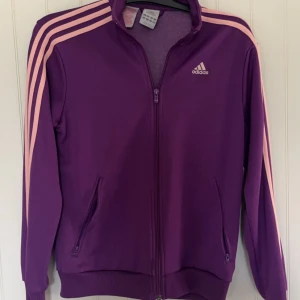 Adidas zip up - Bra skick, något trögt vid ett visst ställe på dragkedjan men går att dra upp hela vägen! Står Stl L men sitter något mindre, typ stl M!  Ränderna på armarna ser rosa ut, var så när jag köpte den!  Skriv helst innan köp.  Djur finns i hemmet! 