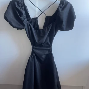 Öppenryggad klänning - Lite festligare svart klänning om man inte är blyg. Öppenryggad och öppen vid sidan av kroppen. Inte använd, för kort för mig.  Står S men XS?