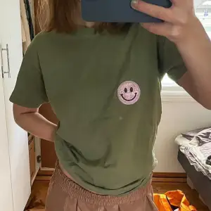 Grön t-shirt med en rosa smiley. Från fruit of the loom, med påstryker patch💓