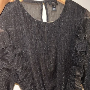 Glittrig blus  - Superfin svart glittrig blus från River Island. Knytning i ryggen. Perfekt till fest! Endast använd 2 gånger så superfint skick. Står storlek 8 men skulle säga att den passa XS-S.