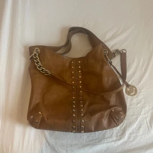 Michel kors  uptown Astor väska  - Vintage Michel kors väska med guld detaljer. Rymmer mycket samtidigt som den är väldigt fin och elegant. Några defekter på tyget i väskan (går och redogöra om man vill de) annars är väskan i väldigt bra skick. Skin.   Dustbag tillkommer 