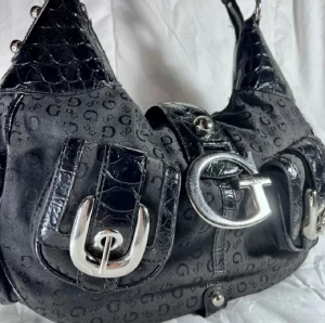 Vintage Guess väska y2k bag  - Äkta Guess väska i fint skick, cirka 34cm bred, 22cm höjd. Canvas och veganskt läder. Texttryck och silverdetaljer. Remmarna är hela och fina. Ligger även uppe hos Vestiaire och Tise