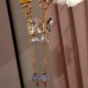 Accessoar till tex nyckel  - Guldkedja med guldhänge (ingen av dessa är äkta guld). Blå glaspärla med guldig hållare. Blå klocka i akryl med vit pärla inuti och genomskinlig akrylfjäril. 